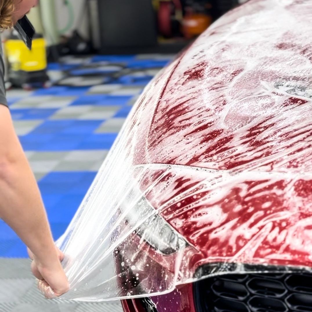 A person is wrapping a red car with plastic wrap