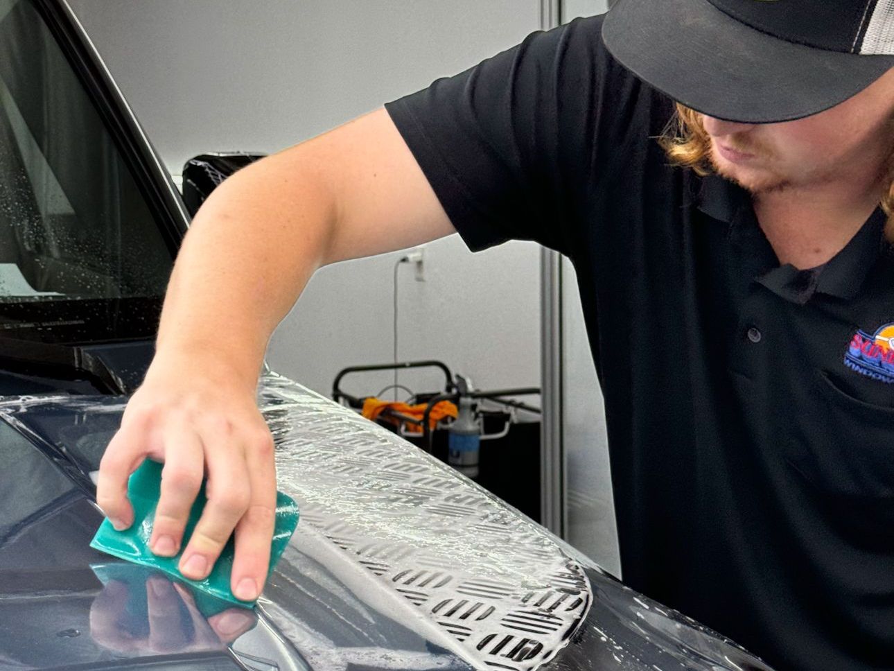 A man wearing a hat is cleaning the hood of a car