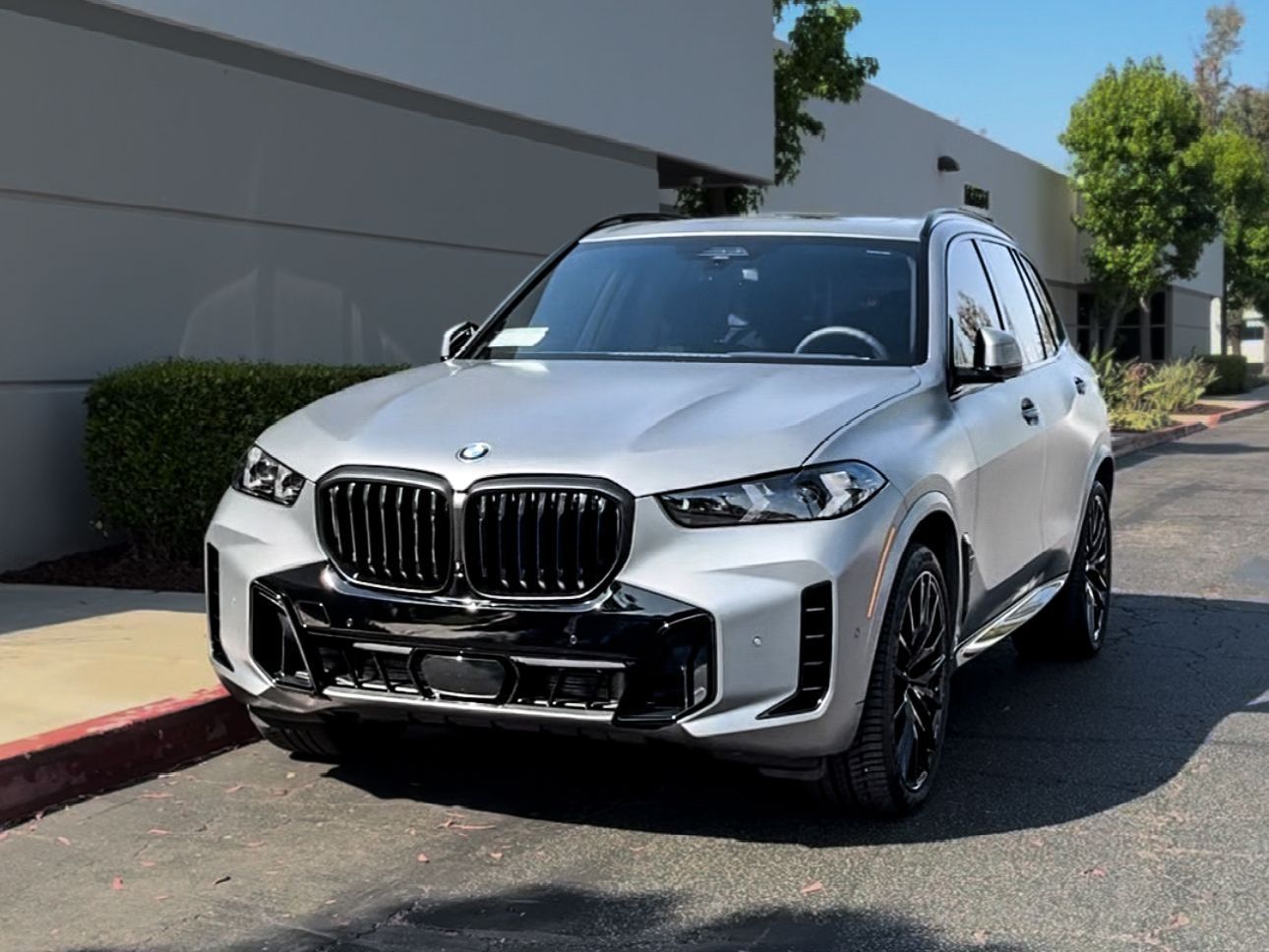 A silver bmw x5 is parked in front of a building.