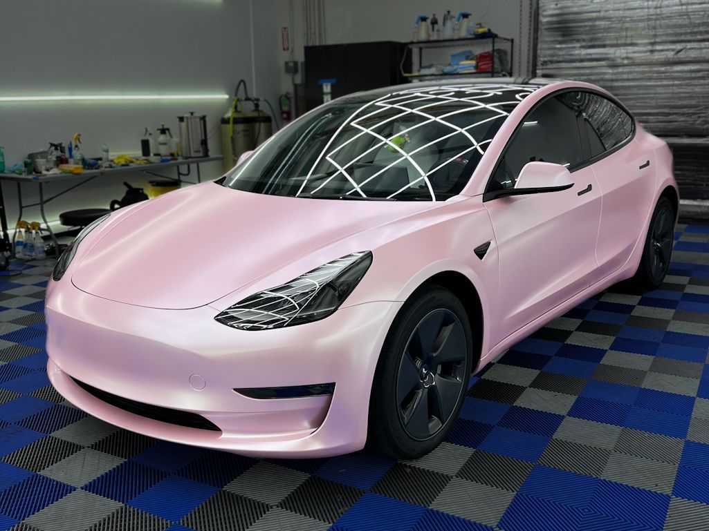 A pink tesla model 3 is parked in a garage.