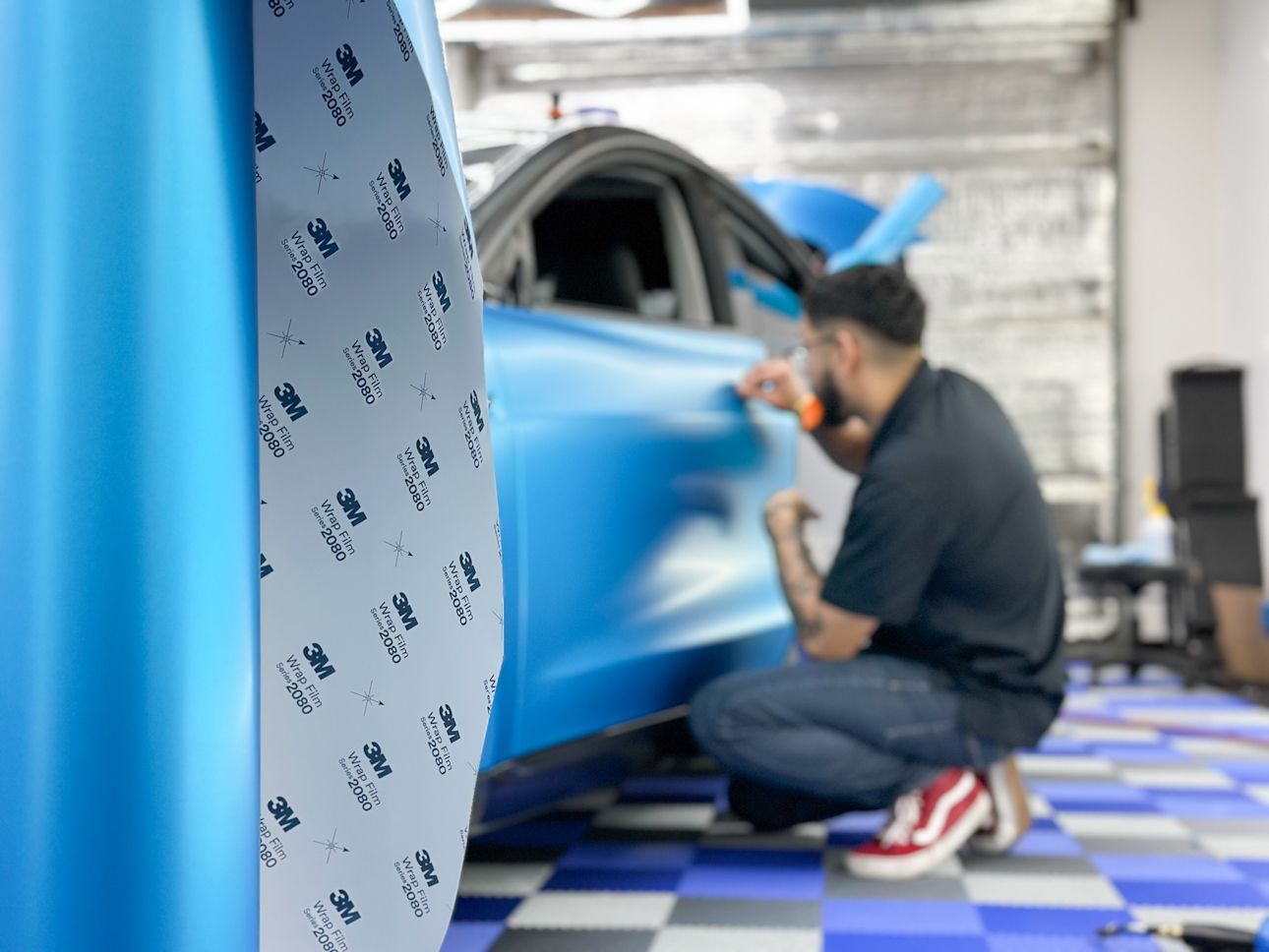 A man is wrapping a blue car in a garage.