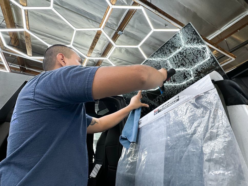 A man in a blue shirt is cleaning a car with a cloth.