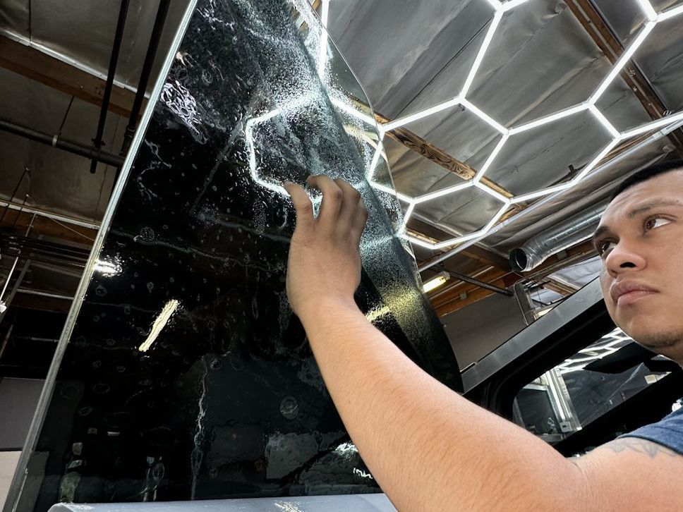 A man is applying a film to the roof of a car.