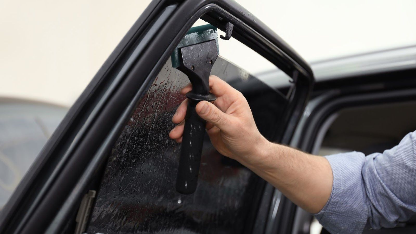 A man is applying tinted window film to a car window.