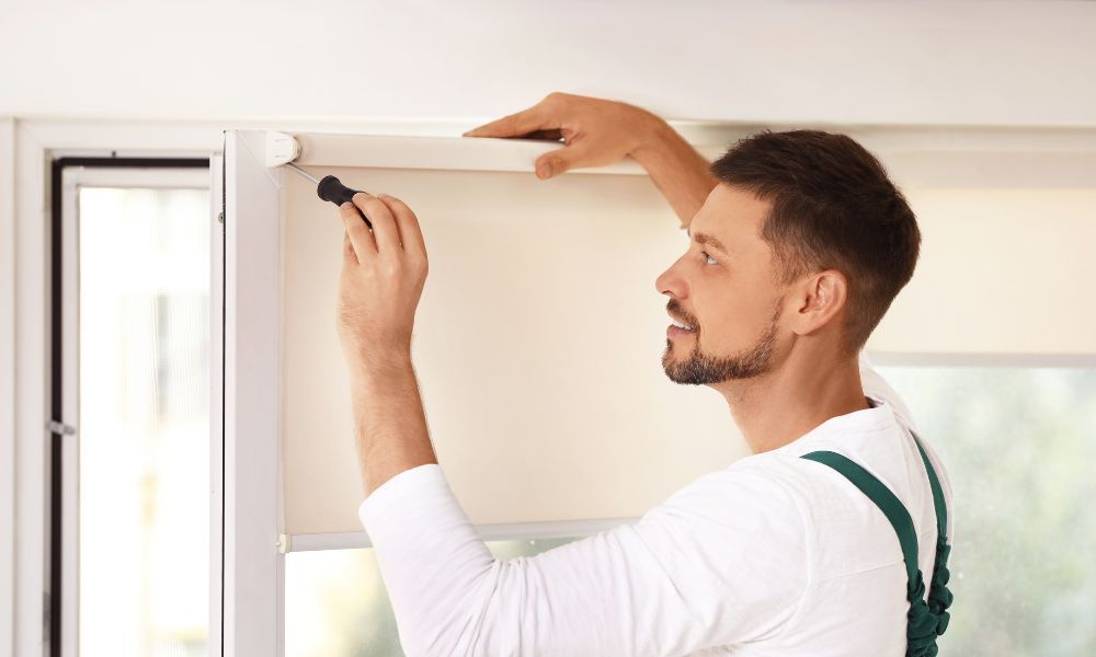 A man is installing blinds on a window.