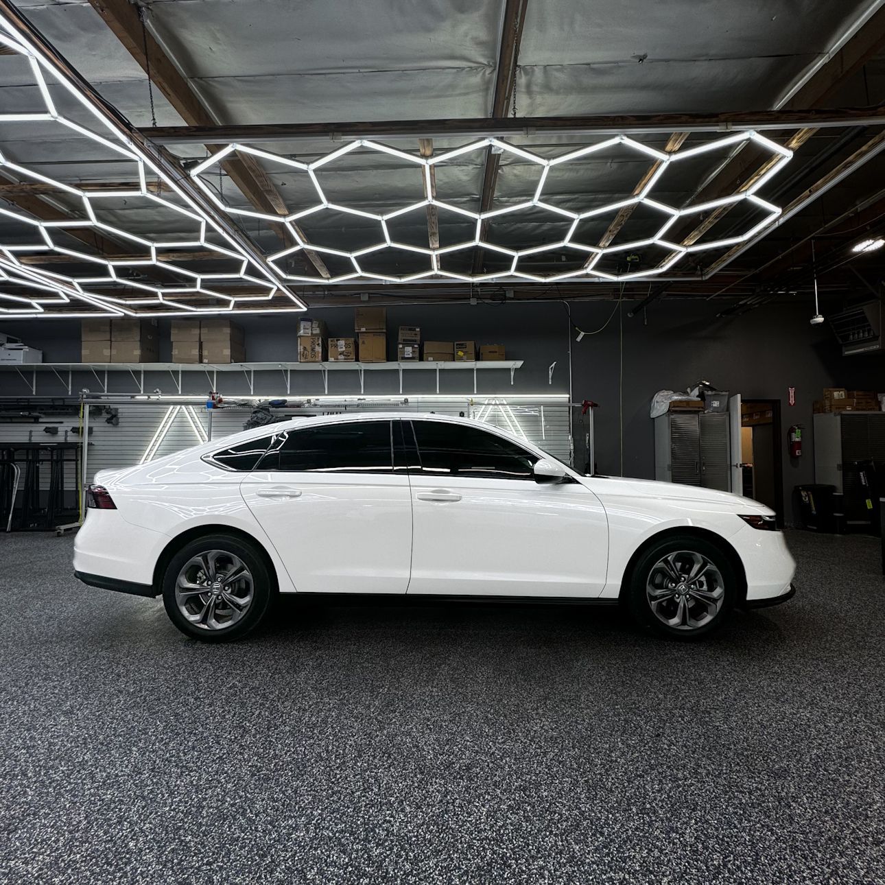 A white car is parked in a garage with a honeycomb ceiling.