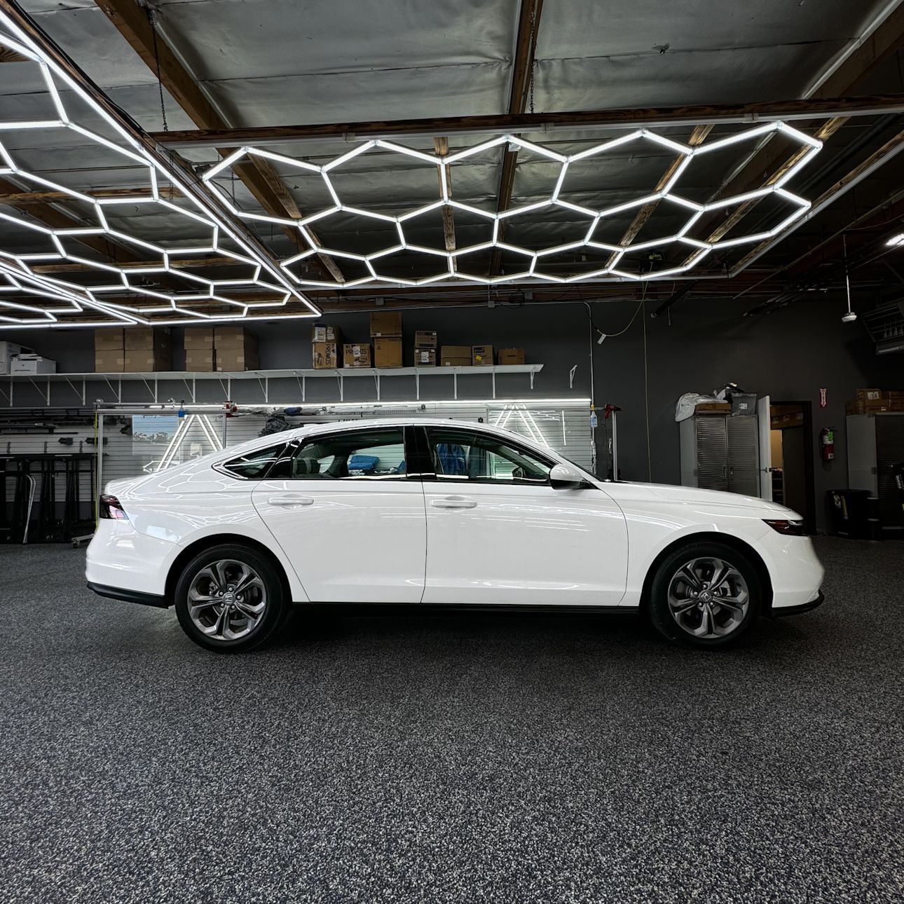 A white car is parked in a garage with a honeycomb ceiling.