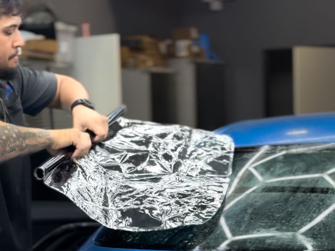 A man is wrapping a blue car with aluminum foil.