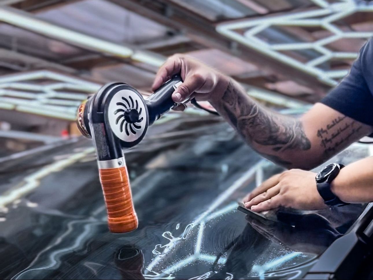 A man is polishing the hood of a car with a polisher.