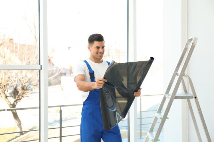 A man in blue overalls is holding a piece of tinted glass.