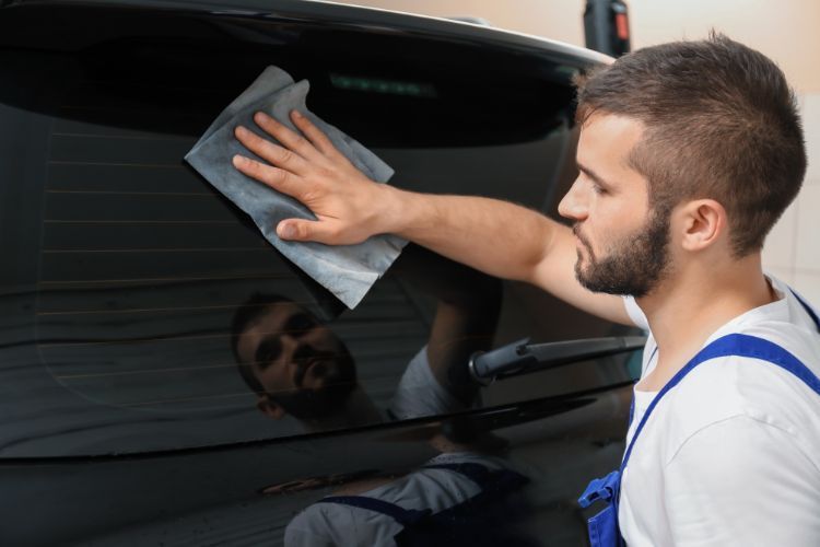 A man is cleaning the back window of a car with a cloth.