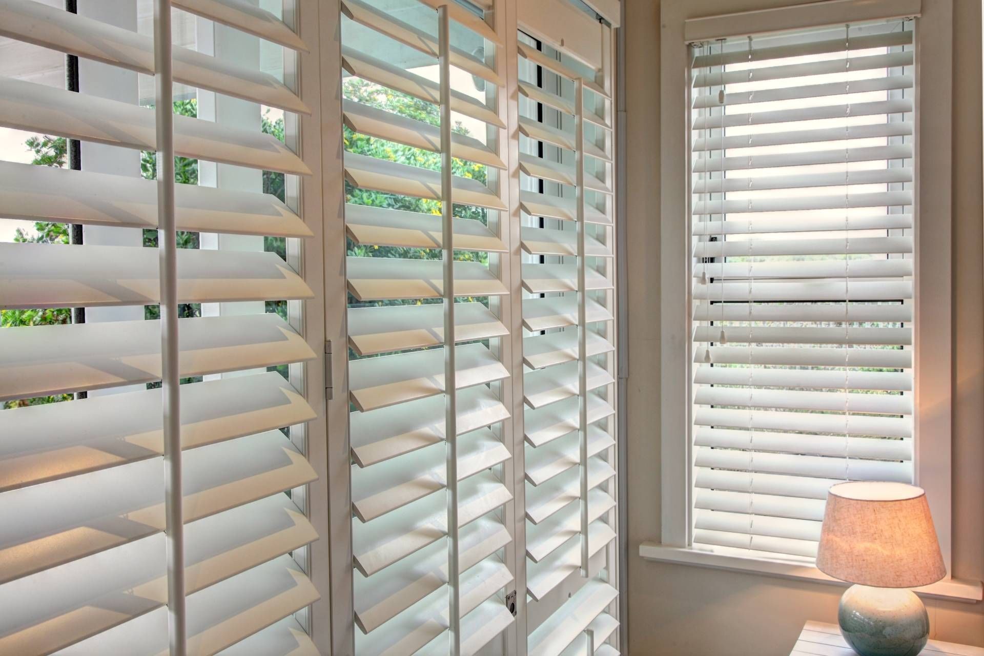 White window shutters with a small lit lamp on a windowsill, daylight filtering through.