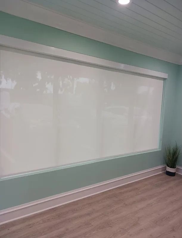 Empty mint-green room with a large whiteboard and wood flooring, plus a potted plant in the corner