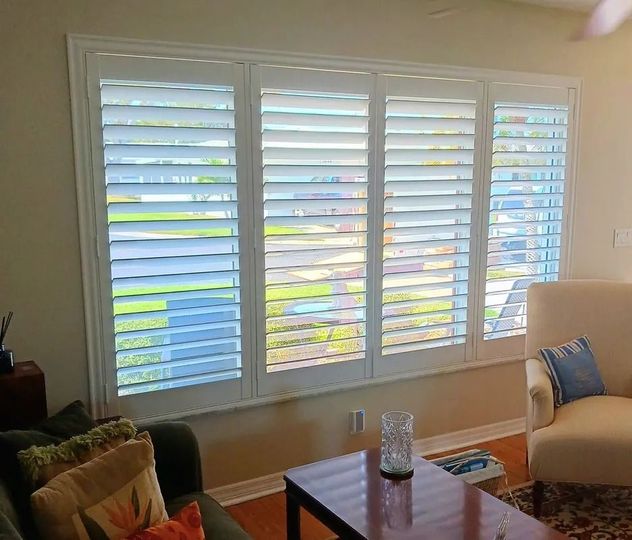 Living room with white plantation shutters, beige sofa, coffee table, and daylight streaming in