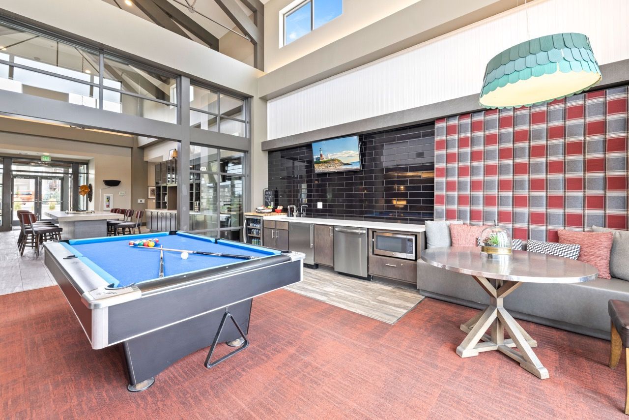 Indoor community lounge with a blue pool table, seating, and a kitchenette.
