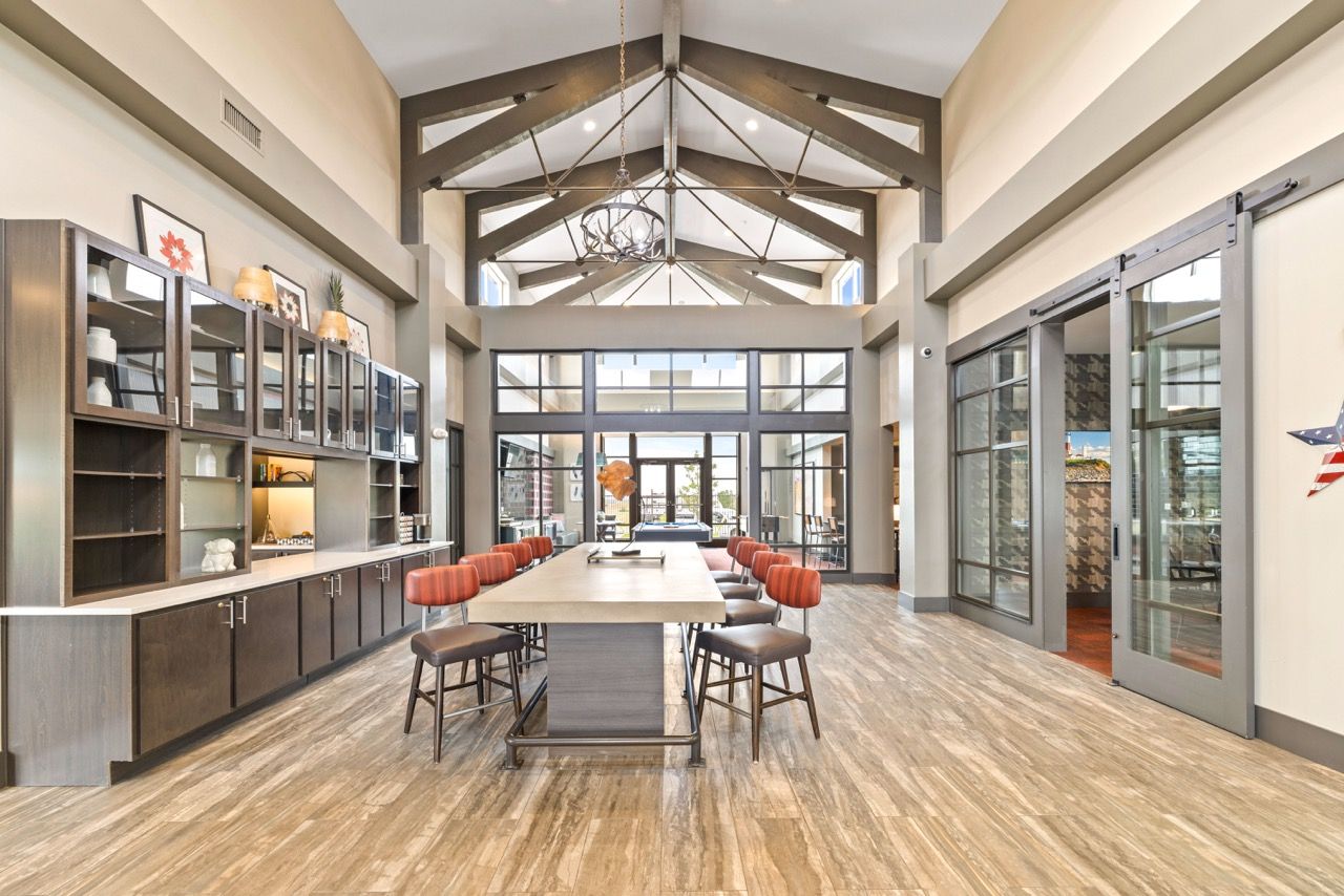 Interior community lounge with a long table, red stools, and glass doors.