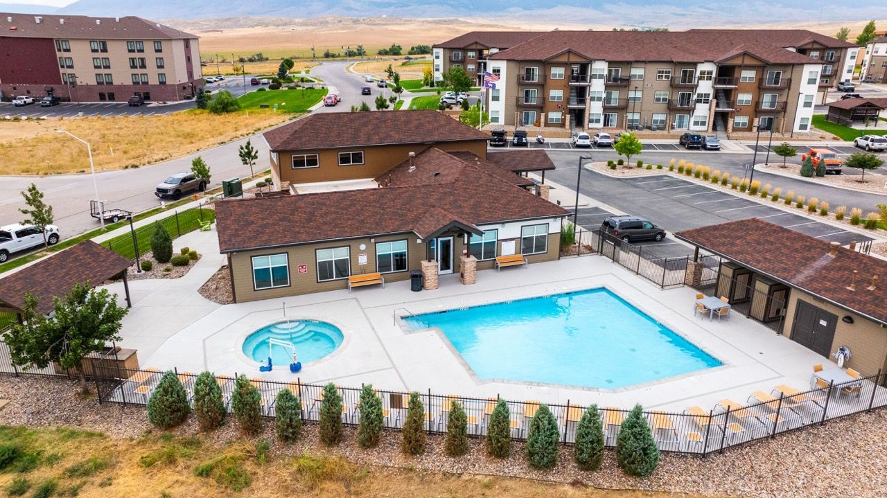 Aerial view of an apartment community pool and spa with a clubhouse and surrounding buildings.