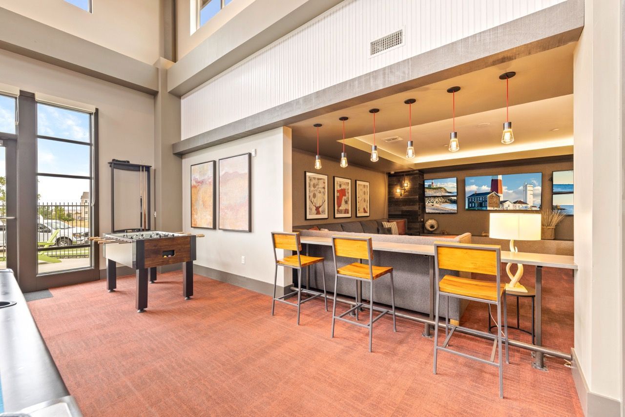 Bright indoor community lounge with a bar-height counter, stools, wall art, and a foosball table.