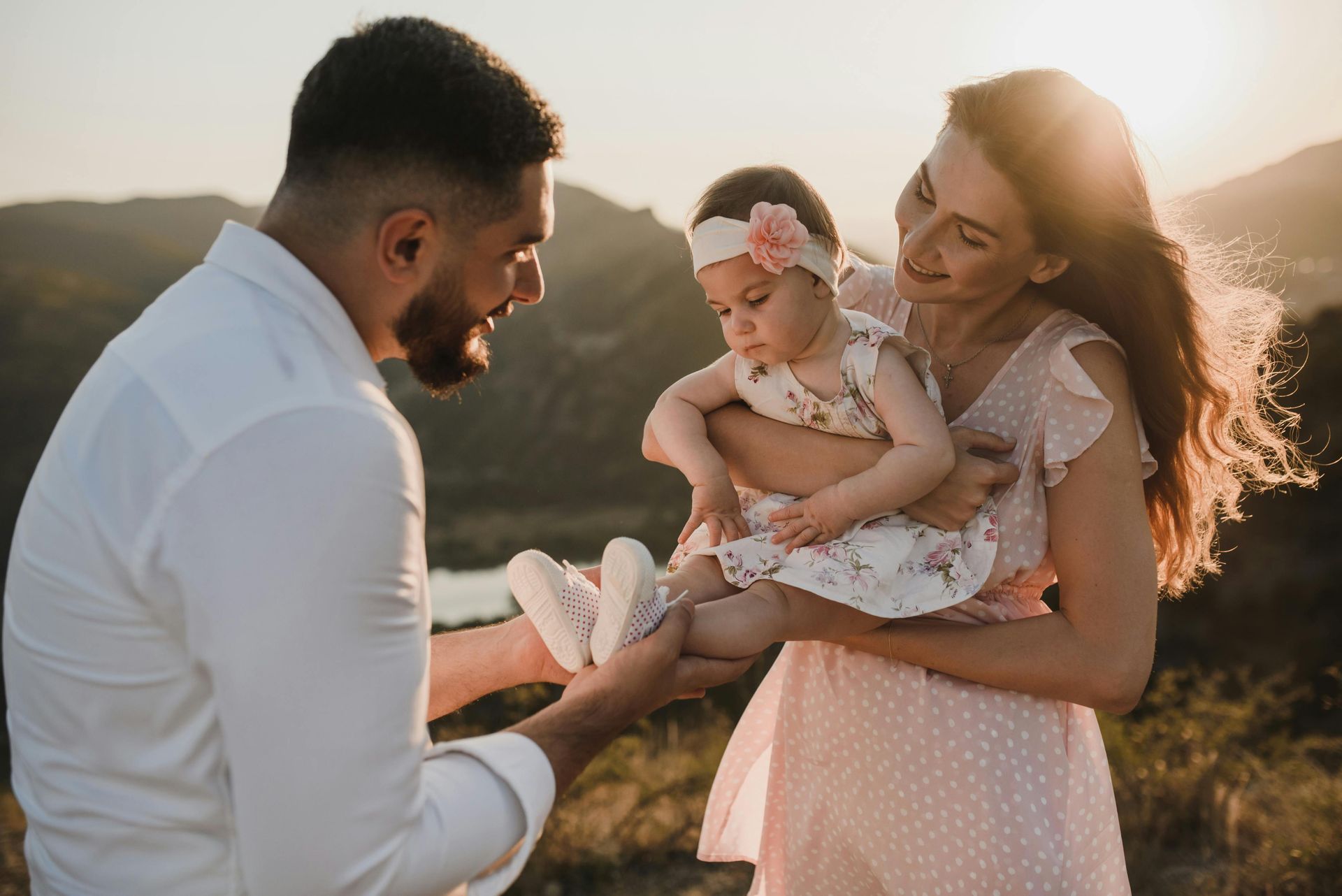 Parents holding a baby outdoors; golden light.