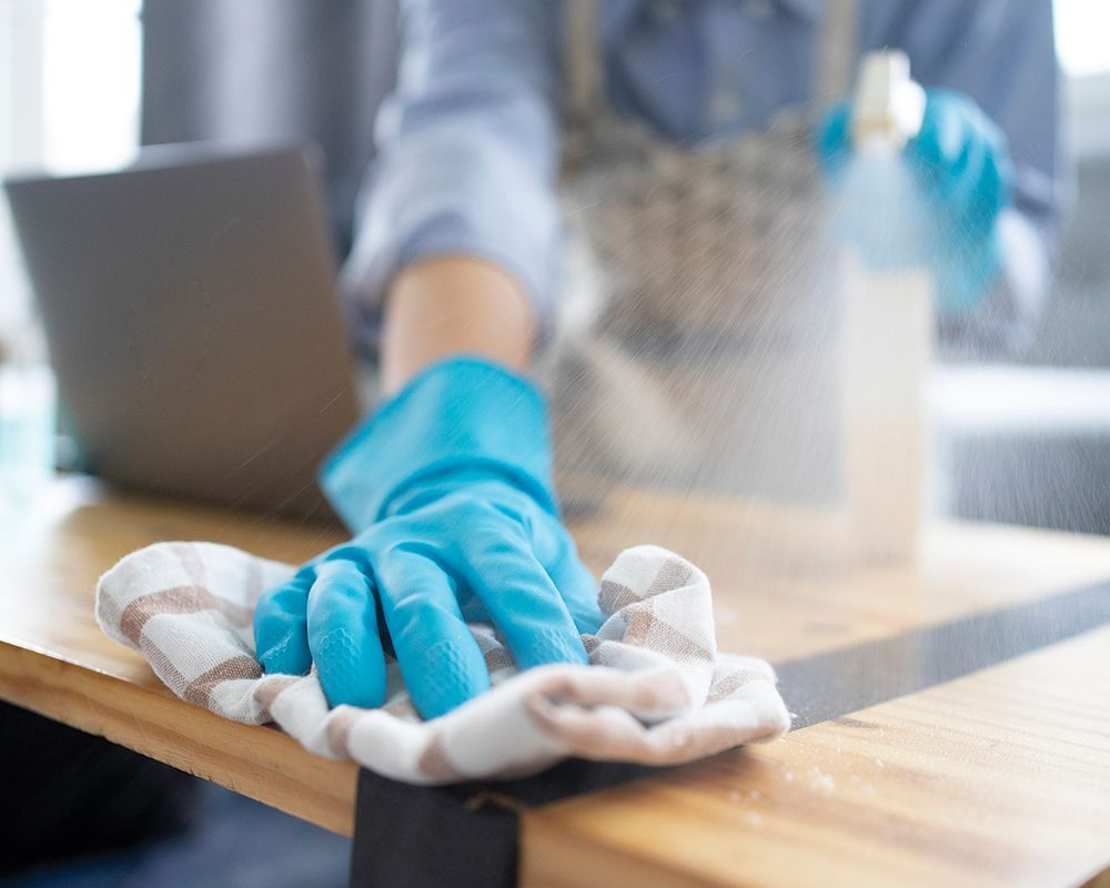A person wearing blue gloves is cleaning a wooden table with a cloth.