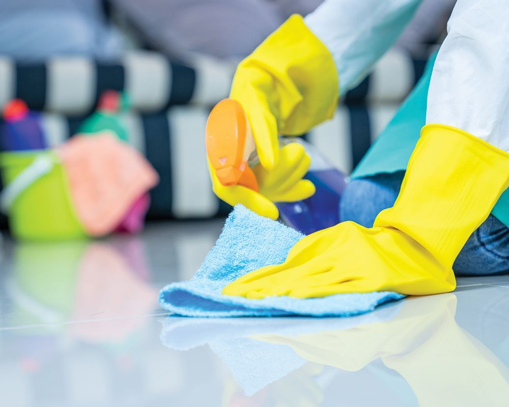 A person wearing yellow gloves is cleaning the floor with a cloth.