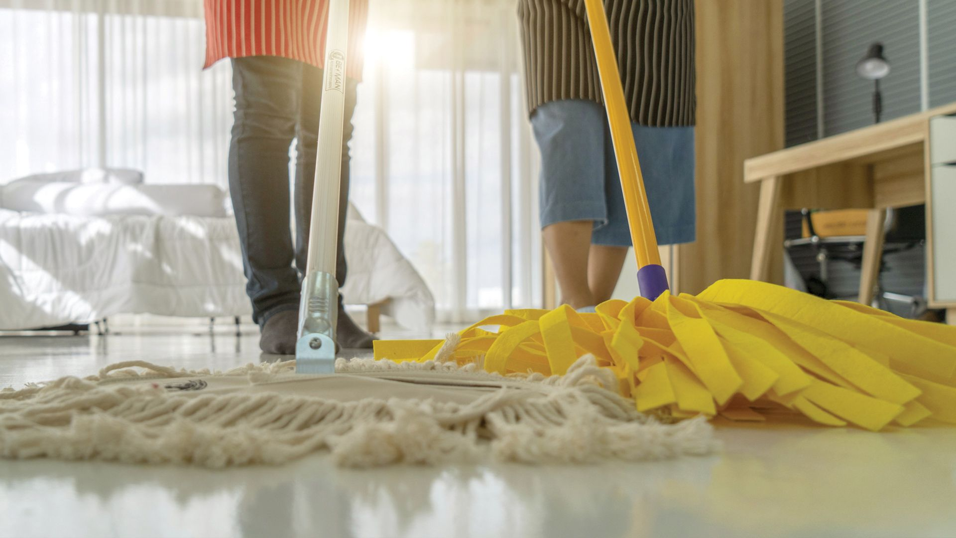 A couple of people are mopping the floor in a living room.