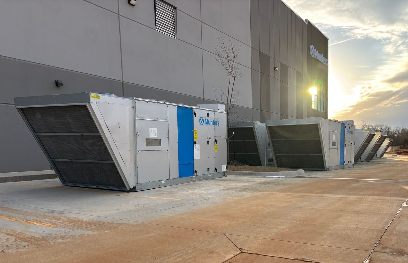 HVAC units outside a building. Gray and blue machines. Sunny outdoor setting.
