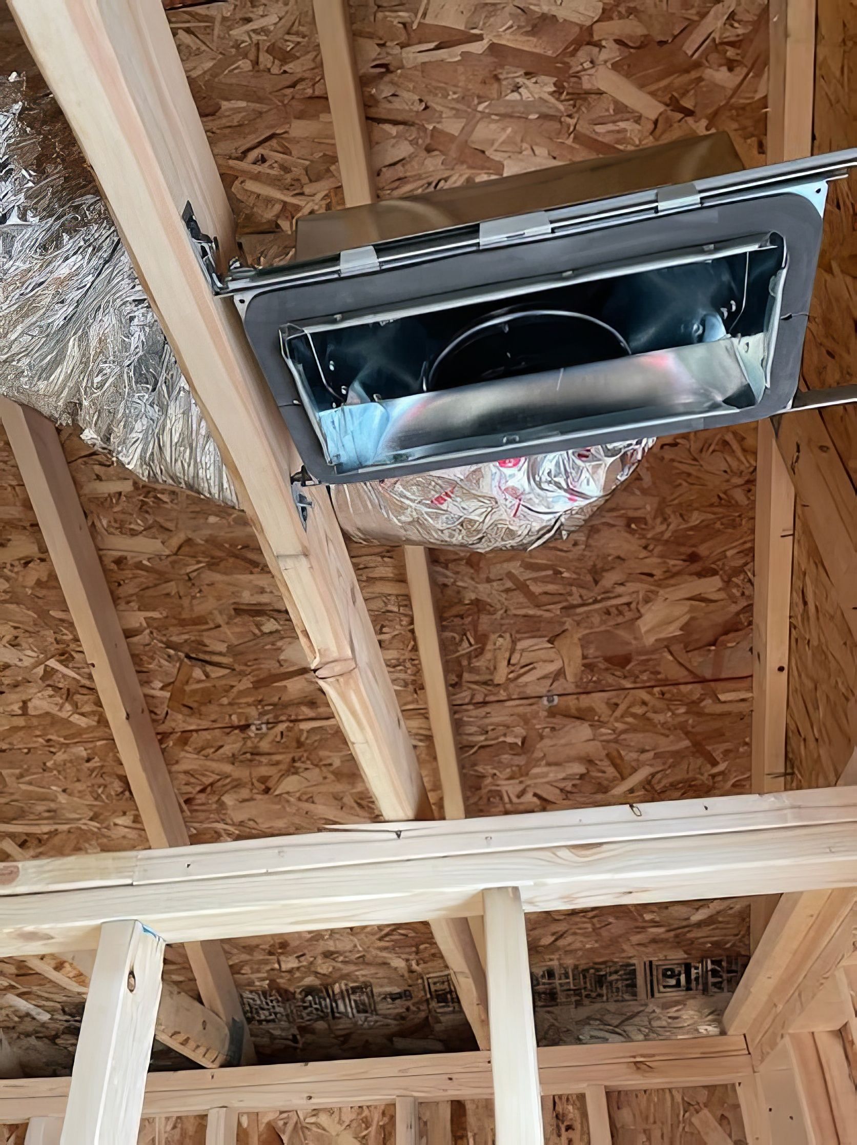 Unfinished ceiling with a rectangular air vent installed between wooden beams.