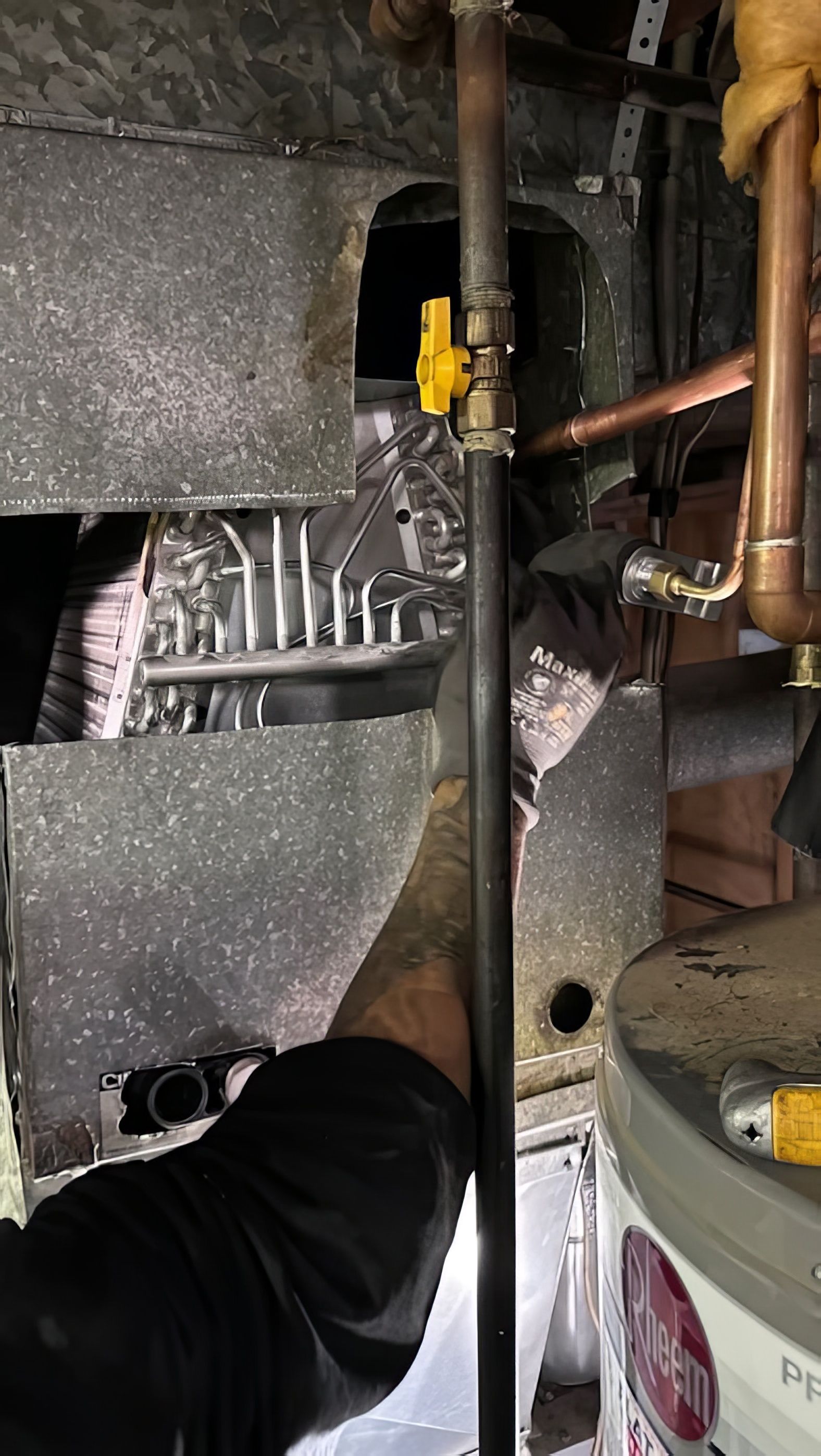 Hand with tools near a furnace. Yellow gas valve and copper pipes.