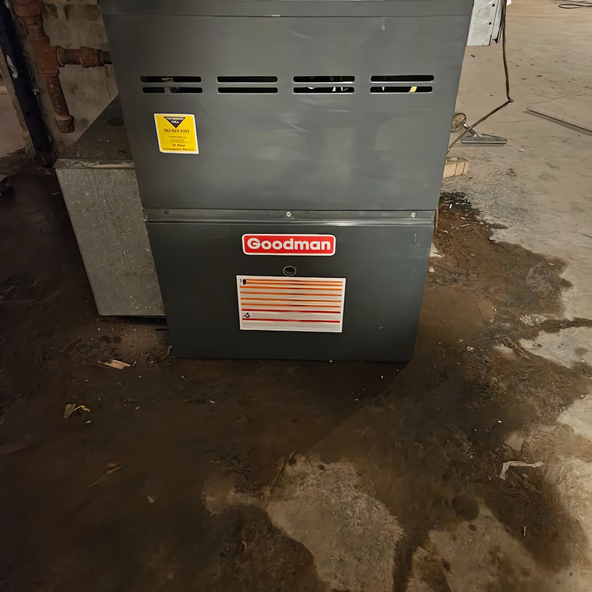 A Goodman furnace in a basement with water on the floor.