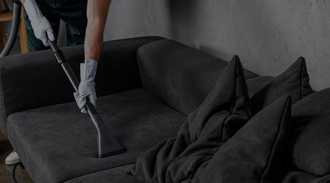 A person is cleaning a couch with a vacuum cleaner.