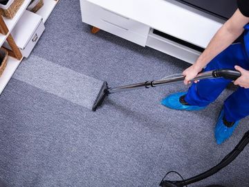 A person is cleaning a carpet with a vacuum cleaner.