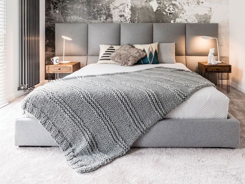 A bed with a grey blanket and pillows in a bedroom