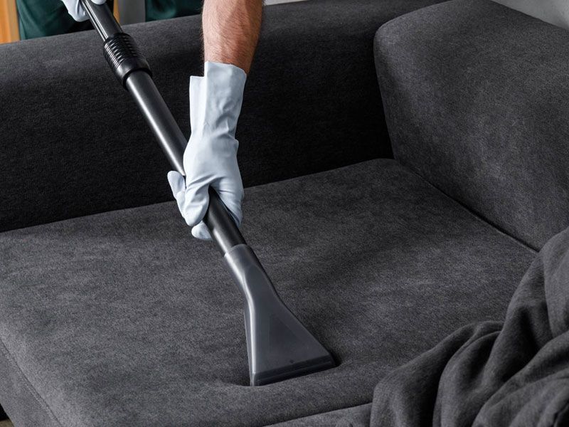 A person is cleaning a couch with a vacuum cleaner.