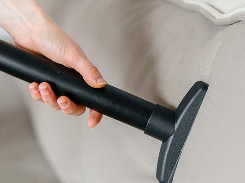 A person is cleaning a couch with a vacuum cleaner.