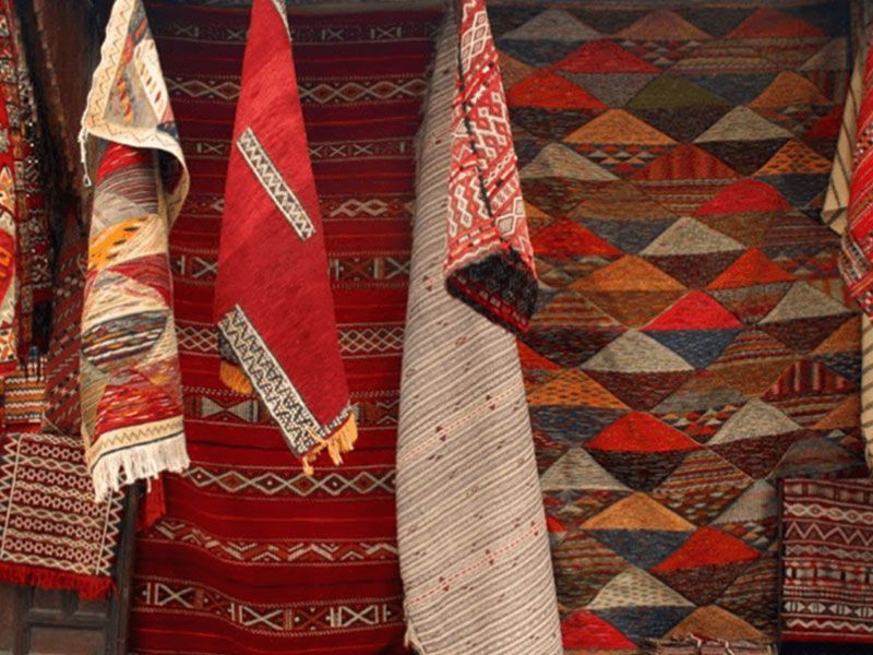 A row of colorful rugs are hanging on a wall