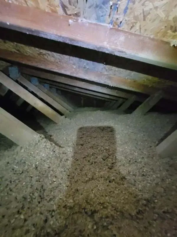 A shadow of a person is cast on the floor of an attic.