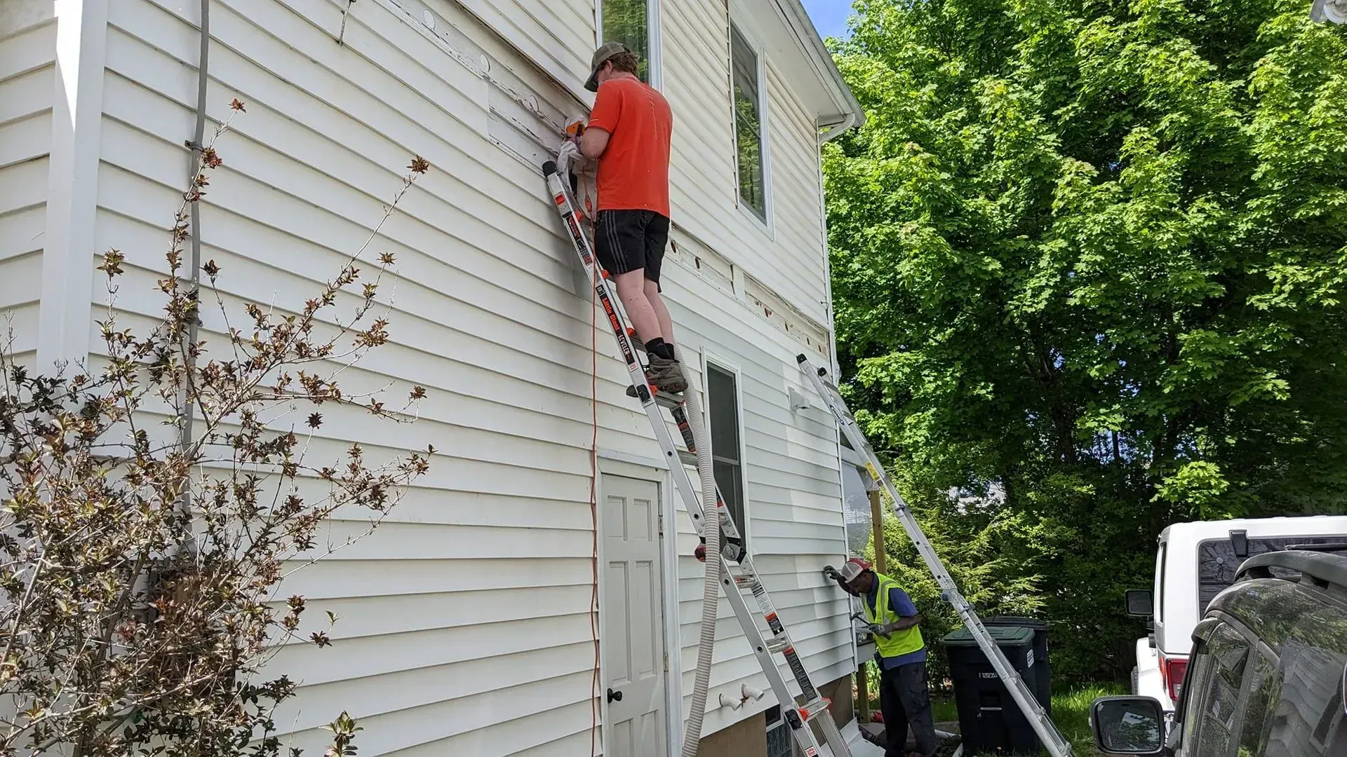 A man is standing on a ladder on the side of a house.