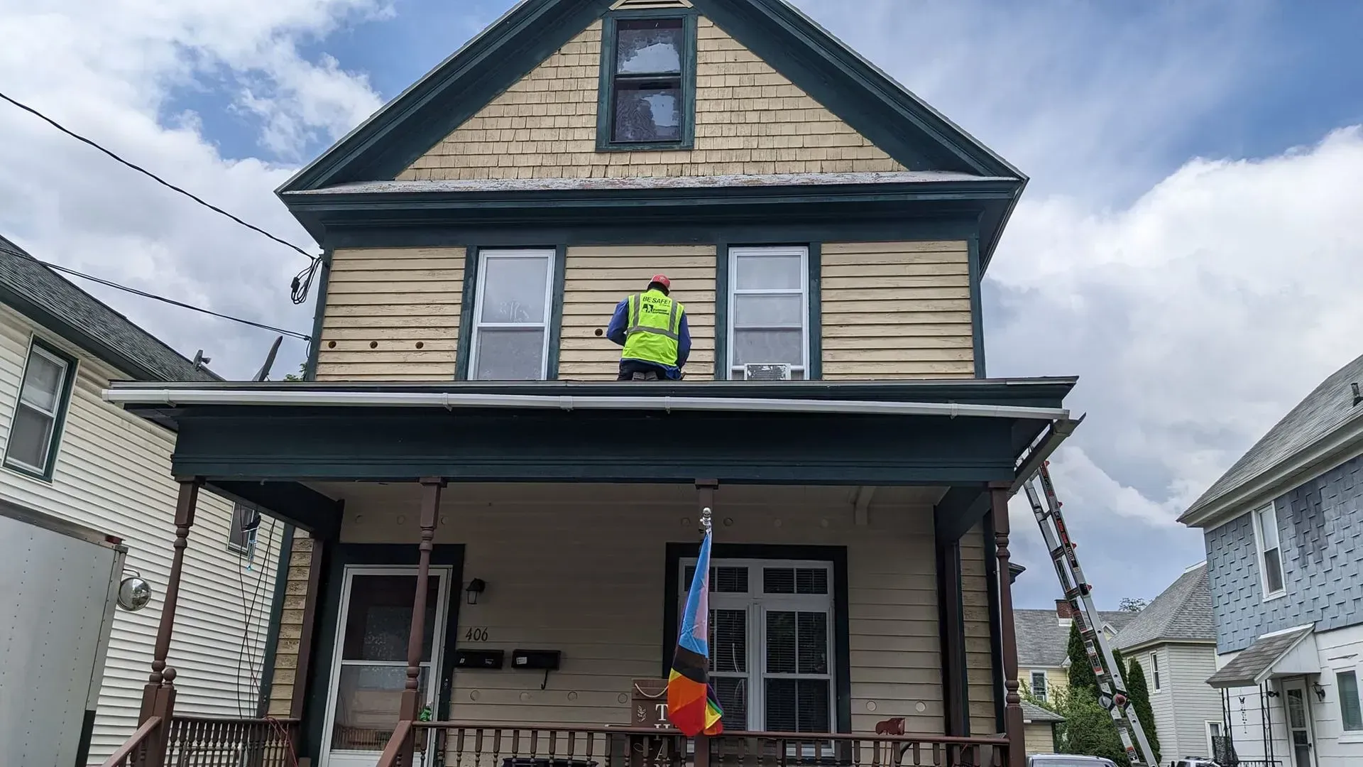 A man in a yellow vest is standing on the roof of a house.