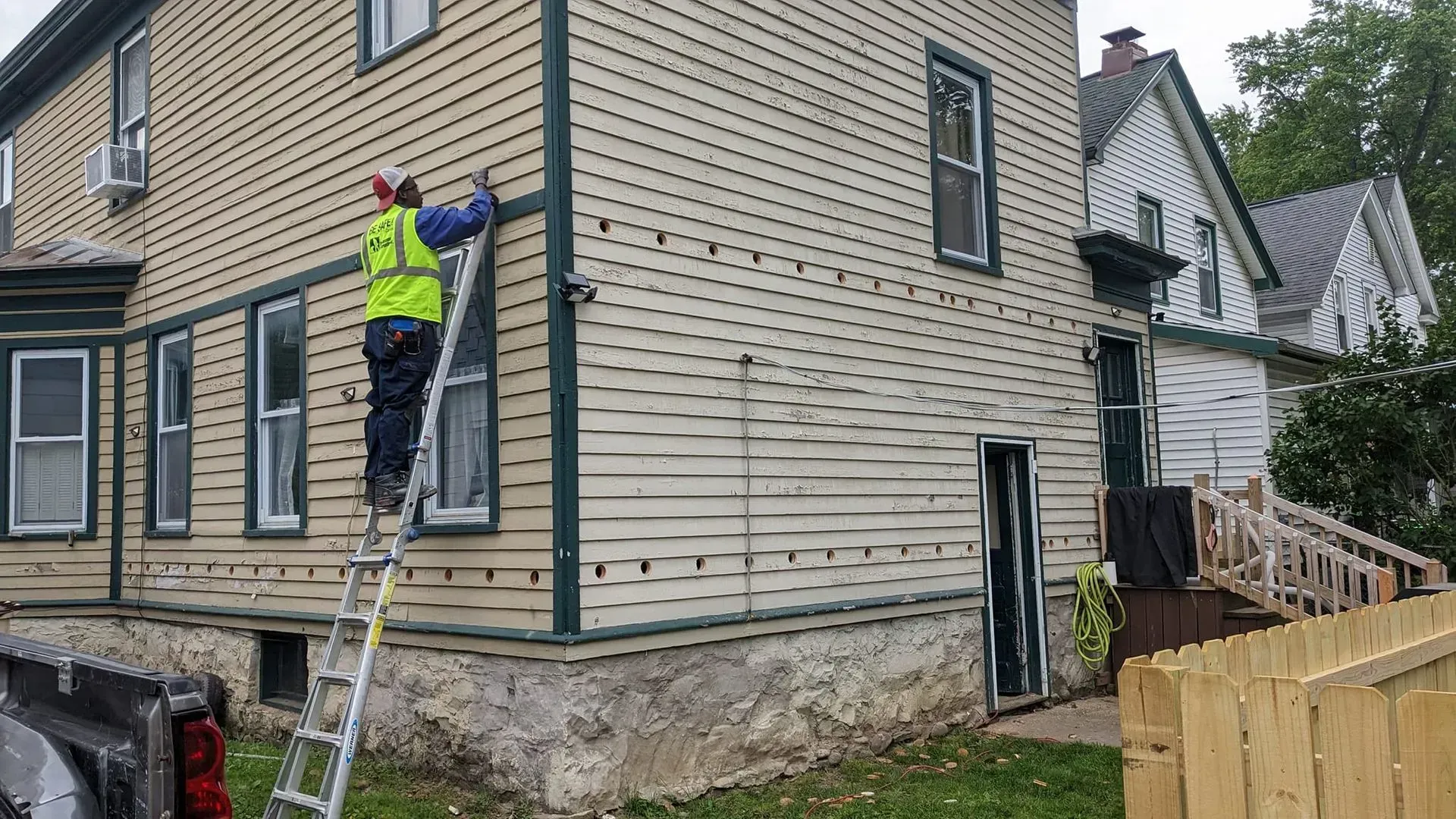 A man is standing on a ladder on the side of a house.