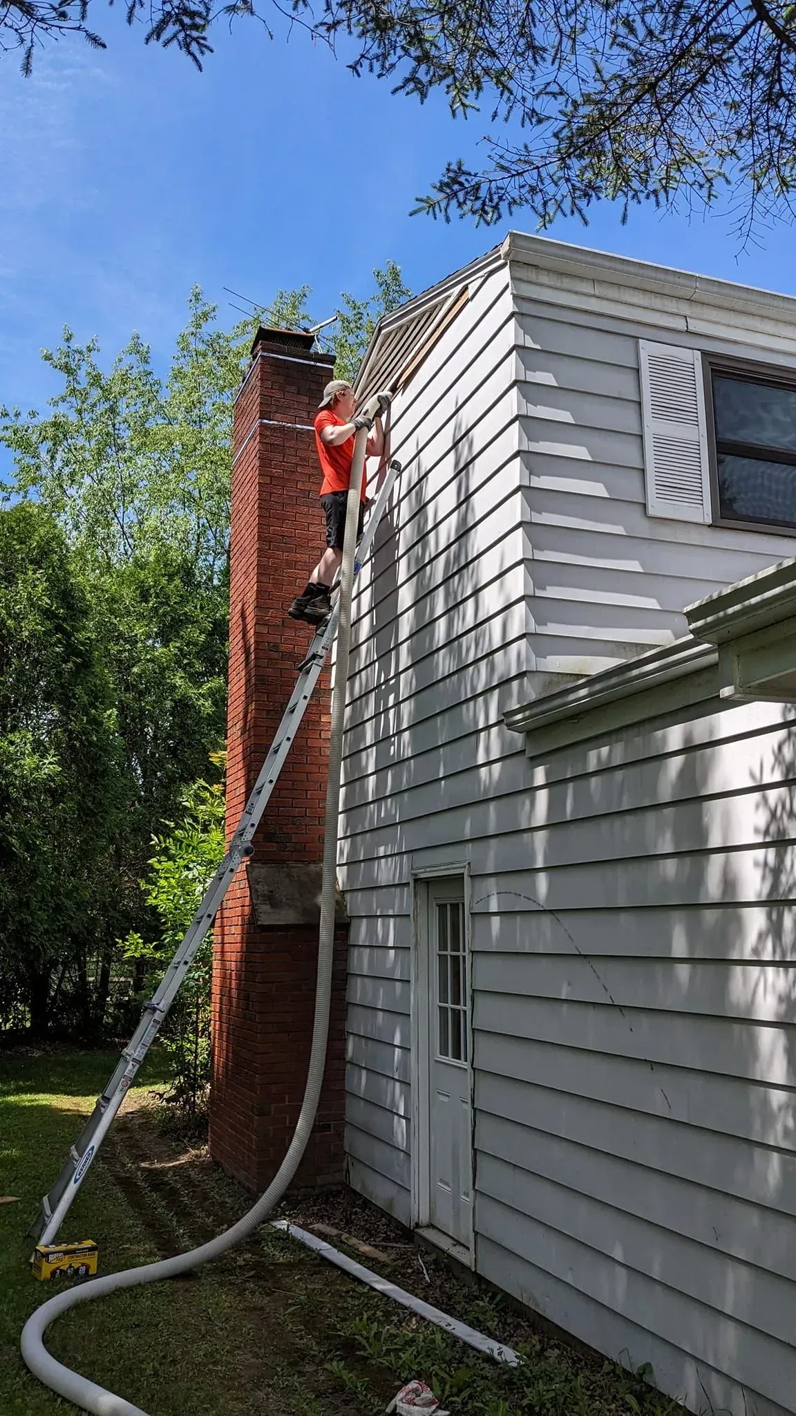 A man is standing on a ladder next to a brick chimney on the side of a house.