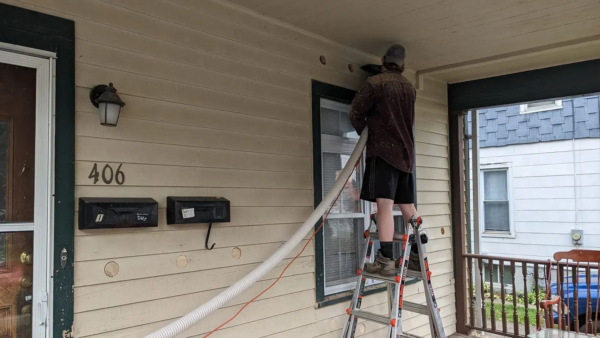 A man is standing on a ladder on the porch of a house.