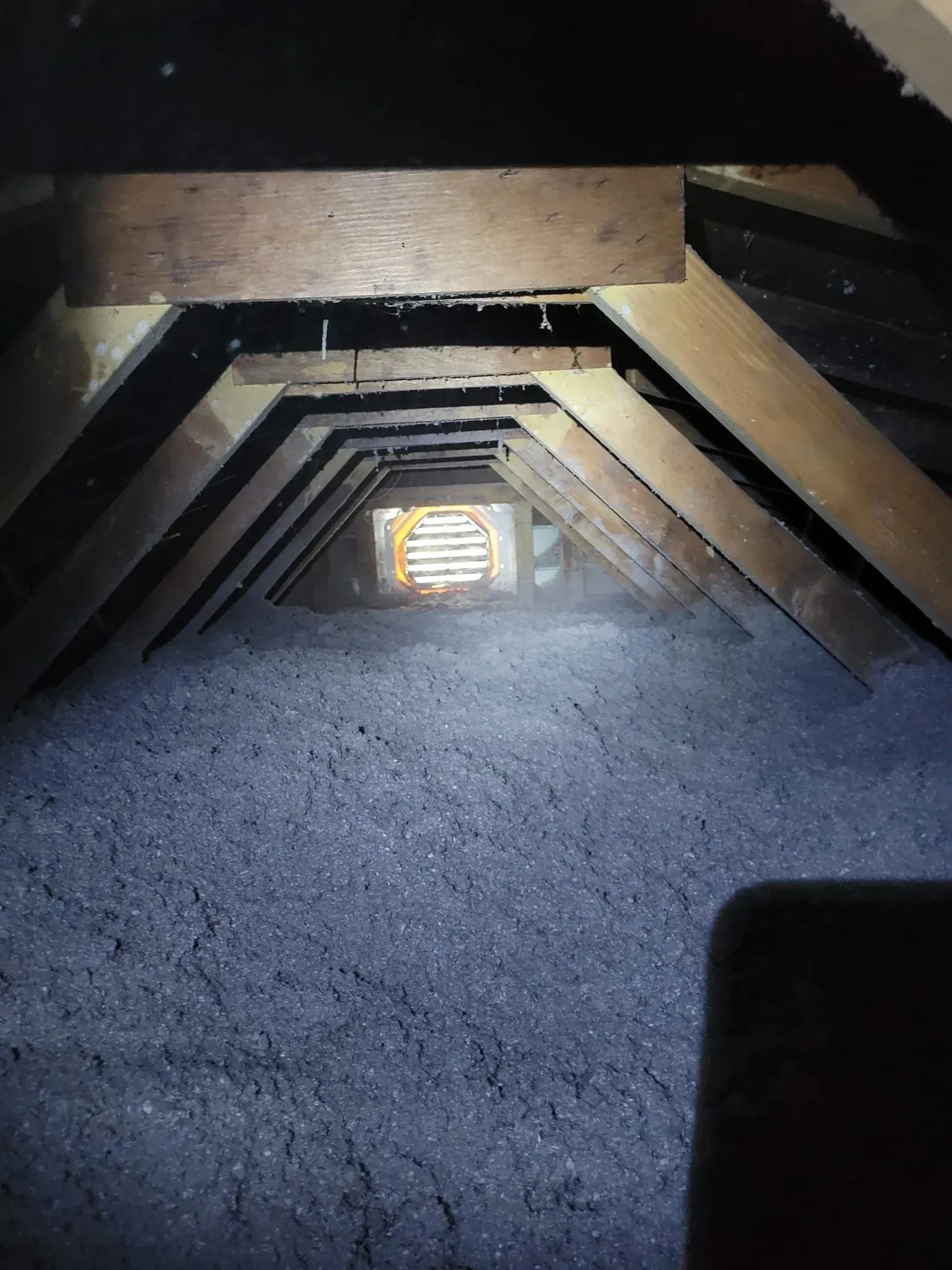 A light is shining through a hole in the ceiling of an attic.