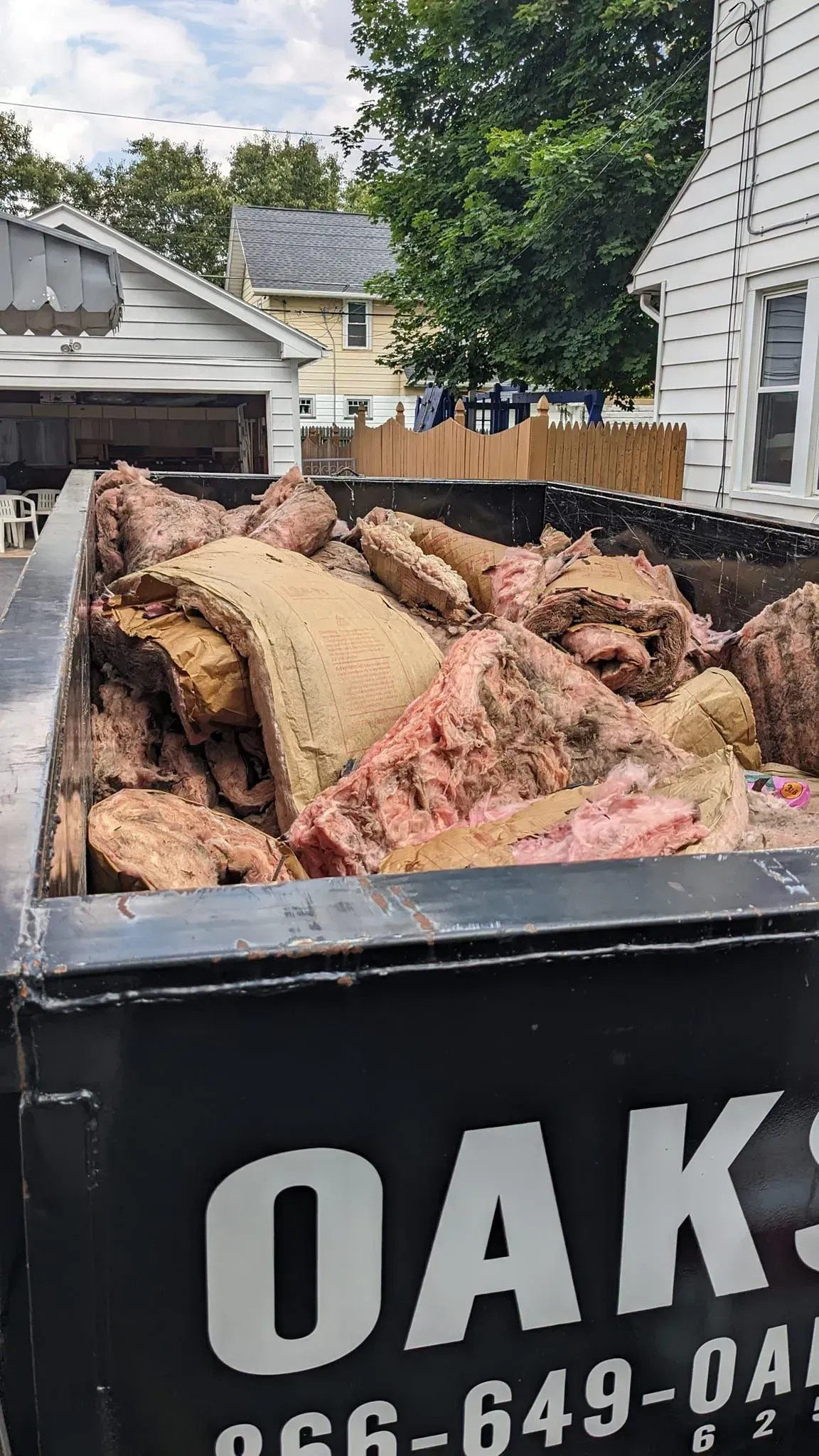 A dumpster filled with a lot of trash is sitting in front of a house.