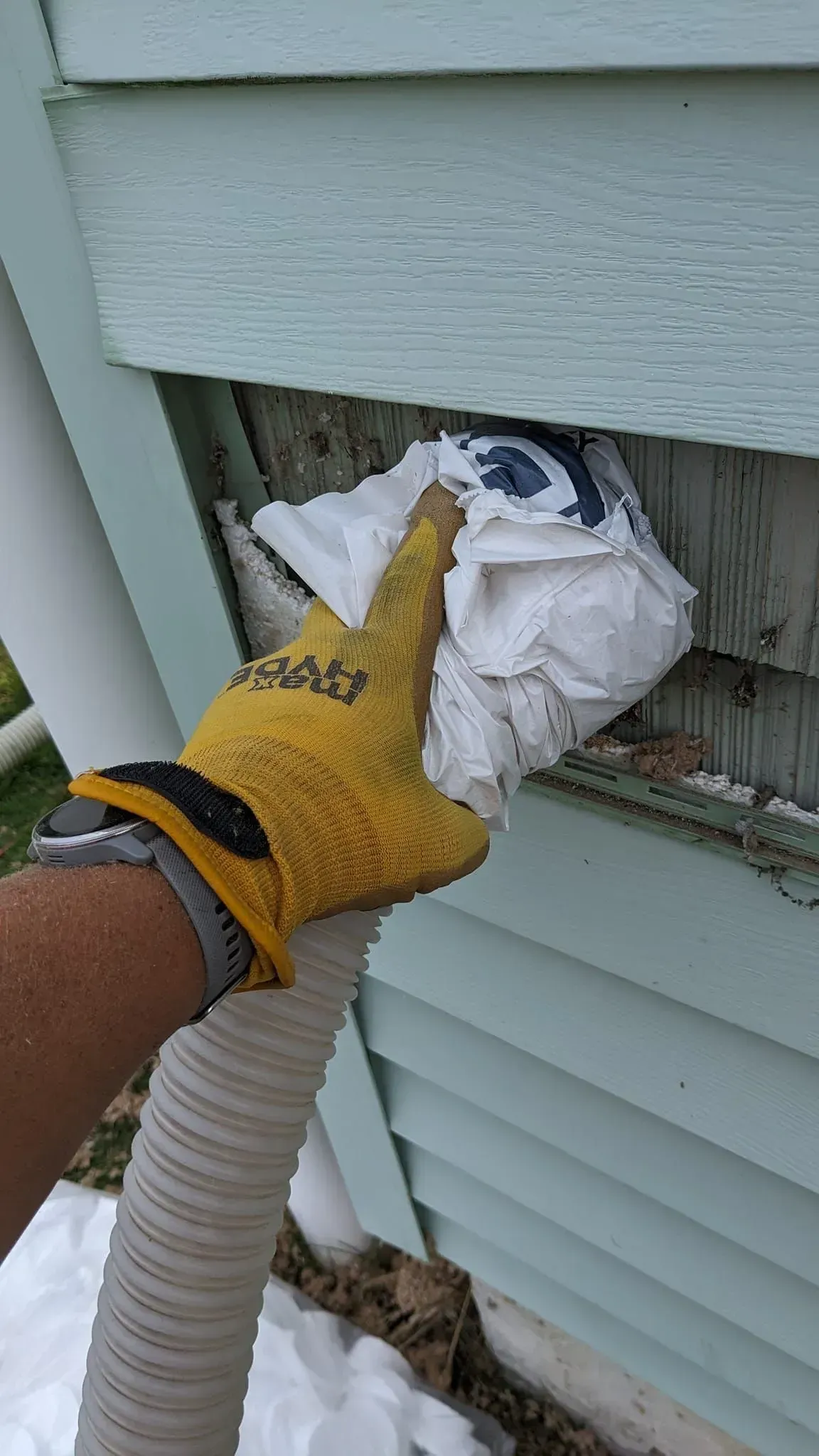 A person is holding a hose and a piece of paper in front of a house.