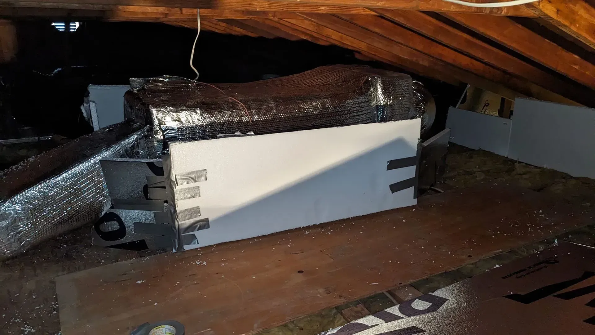 A white box is sitting under a wooden ceiling in an attic.