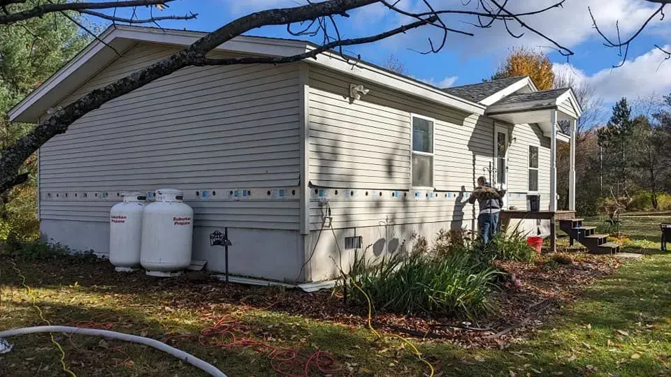 A white mobile home with two propane tanks on the side of it.