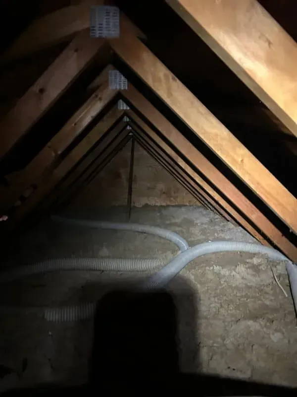 A dark attic with a lot of wooden beams and wires.