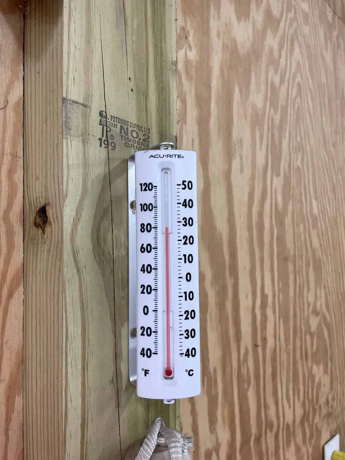 A white thermometer is hanging on a wooden wall.