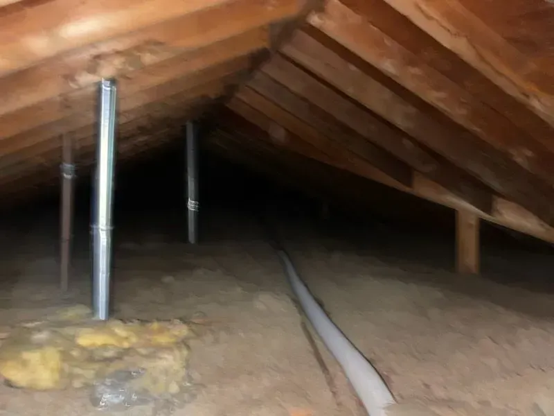 A dark attic with wooden beams and a metal pipe.